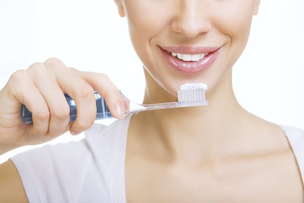 lower half of a woman's face brushing her teeth with whitening toothpaste