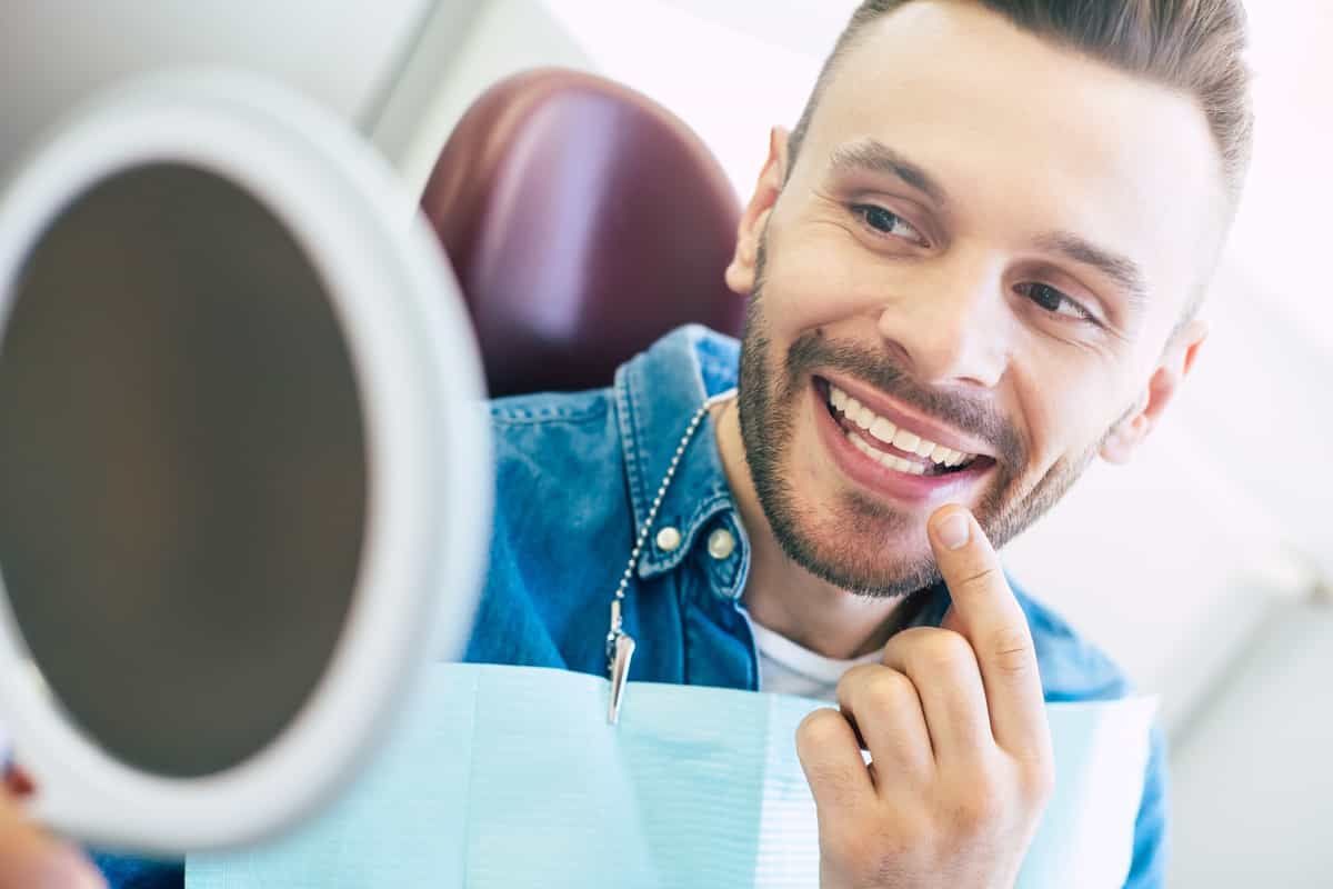man in dentist chair checking his teeth in a mirror